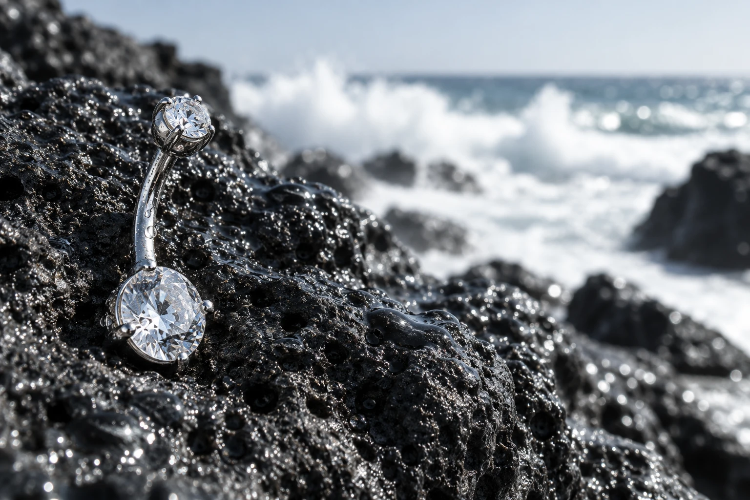 Bijou de nombril en titane à deux cristaux sur une roche volcanique mouillée, vagues en arrière-plan